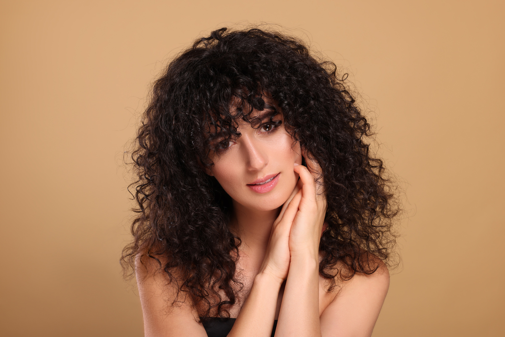 Beautiful Young Woman with Long Curly Hair on Beige Background